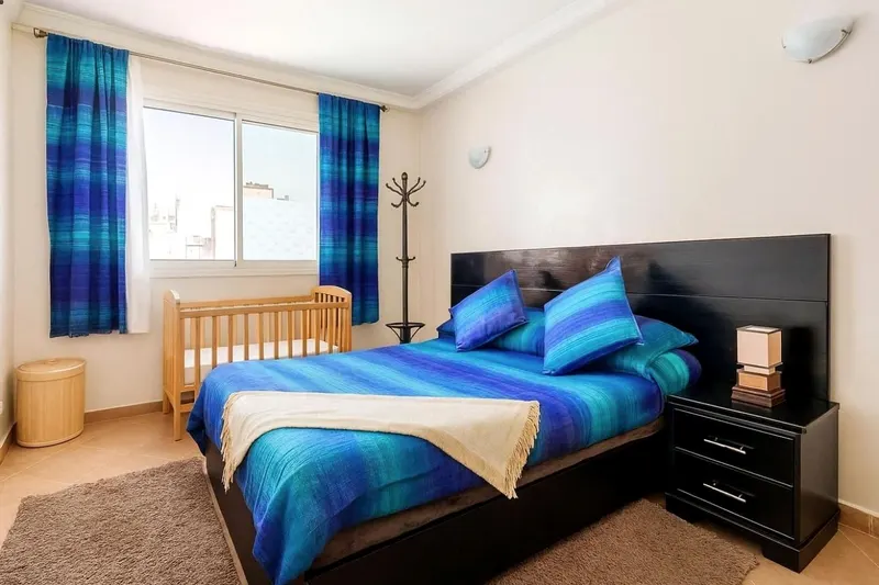 Bedroom: a large double bed with a cobalt striped blanket, blue curtains and a baby cot