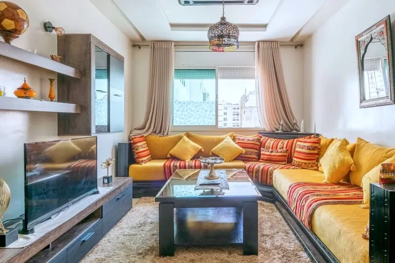 Salon 1: an L-shaped Moroccan banquette in saffron and red stripes, a low table, a TV and a brass lantern